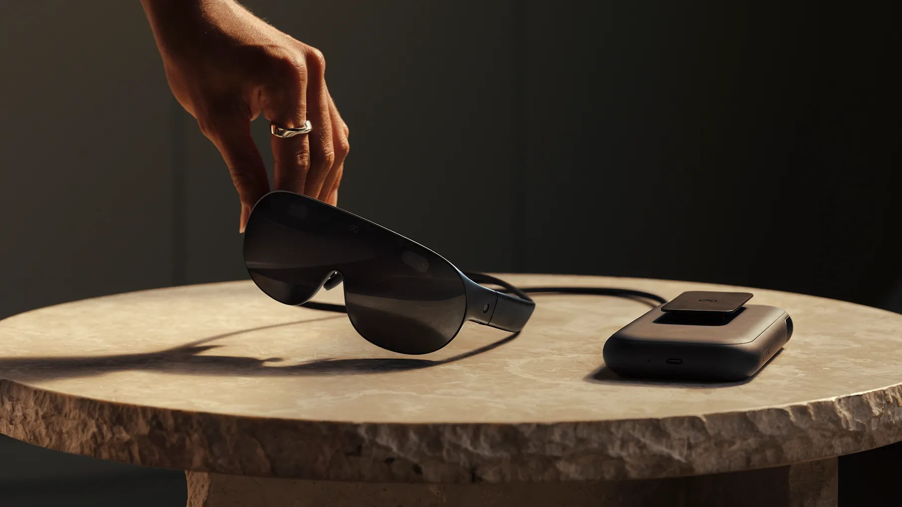 A hand lifting the Meta VR Glasses from a table next to its external compute puck, revealed at Meta Connect 2026.